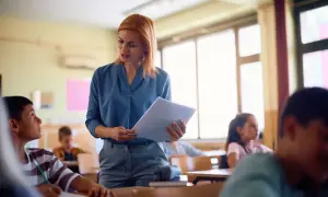 Nauczycielka z dokumentami w ręku omawia projekt oceny dorobku zawodowego na nauczyciela mianowanego z uczniami w klasie.