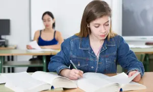 Dziewczyna w dżinsowej kurtce pisze notatki, przygotowując się do egzaminu poprawkowego.