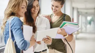 Trzy studentki przeglądają notatki na tablecie, przygotowując się do matury. Lektury obowiązkowe matura - wspólna nauka.