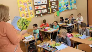Nauczycielka czyta dzieciom książkę, podczas gdy uczniowie siedzą przy ławkach. To może być dzień składania wniosku o przyjęcie do szkoły podstawowej.