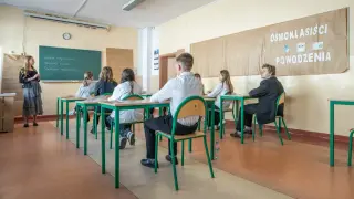 Uczniowie siedzą w ławkach, gotowi do egzaminu ósmoklasisty. Na tablicy widnieje napis "Powodzenia!".