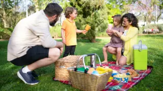 Radosny piknik rodzinny w parku. Rodzice i dzieci cieszą się wspólnym czasem na kocu, wśród zieleni.