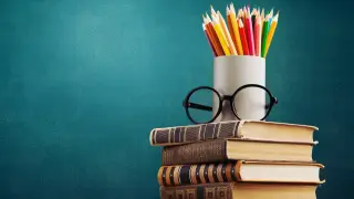 Stos książek, okulary i kolorowe kredki na tle tablicy. Nawet bez matury można zdobyć wykształcenie średnie.