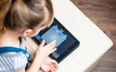 Dziecko dotyka ekranu tabletu z ikonami aplikacji społecznościowych, w tym Facebooka. Od ilu lat można mieć Facebooka?