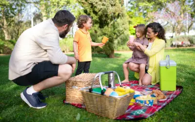 Radosny piknik rodzinny w parku. Rodzice i dzieci cieszą się wspólnym czasem na kocu, wśród zieleni.