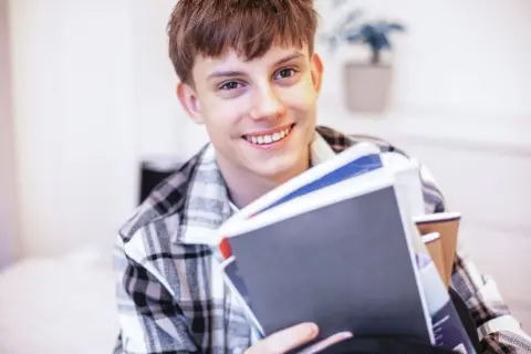 Uśmiechnięty student z książkami, zastanawia się, jak rozliczyć dochody dziecka pełnoletniego uczącego się.