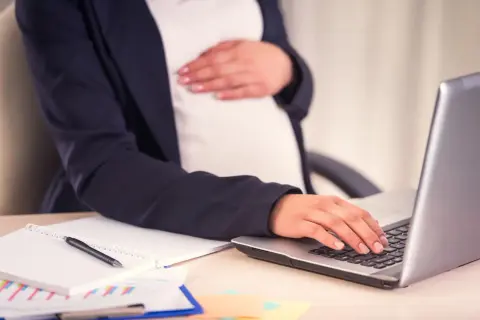 Kobieta w ciąży przygotowuje wniosek o urlop macierzyński, pracując przy laptopie.
