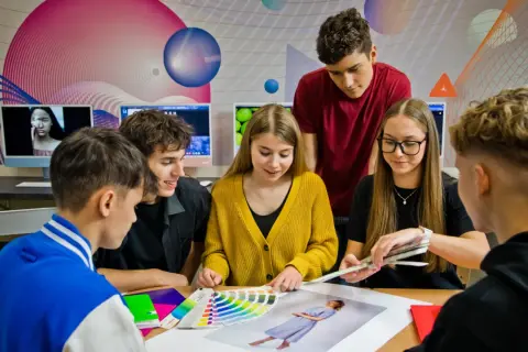 Młodzi ludzie, przyszli **technicy reklamy**, analizują palety kolorów i projekty.