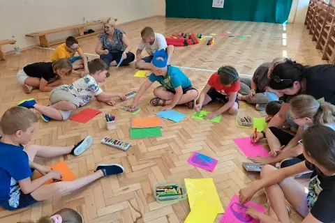 Dzieci klas 1-3 biorą udział w zabawach integracyjnych, rysując na kolorowych kartkach.