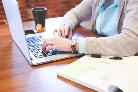 Osoba pracuje na laptopie, studiując różne rodzaje wykształcenia. Na biurku leży notatnik i kubek z herbatą.