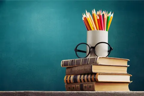 Stos książek, okulary i kolorowe kredki symbolizują drogę do wiedzy, która zaczyna się od wykształcenia średniego.