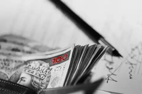 Stos banknotów 100 zł w portfelu, obok pióro i zapiski. FGŚP.