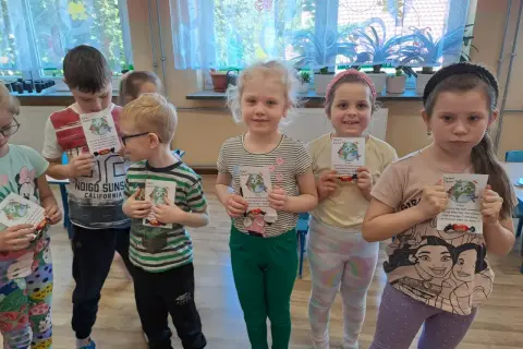 Dzieci z oddziału przedszkolnego świętują Dzień Ziemi, trzymając w rękach kartki z motywem planety i słodkości.