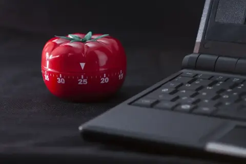 Czerwony minutnik w kształcie pomidora obok klawiatury laptopa, gotowy do pracy metodą pomodoro.