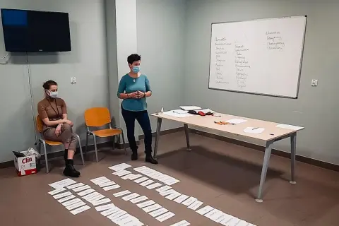 Trening zastępowania agresji: dwie kobiety w maseczkach, tablica z zapiskami, kartki na podłodze.