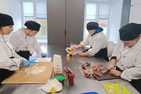 Uczniowie na kierunku technik żywienia i usług gastronomicznych ćwiczą krojenie kiełbasy i przygotowanie ciasta.
