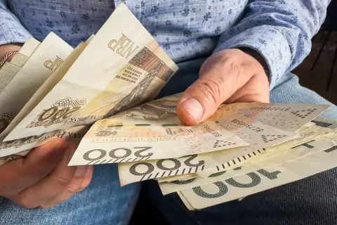 Dłonie trzymają polskie banknoty 200 zł i 100 zł. Zastanawiasz się, czy 800 plus wlicza się do dochodu?