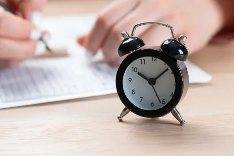 Budzik obok arkusza egzaminacyjnego. Czas na egzamin ósmoklasisty tyka nieubłaganie.