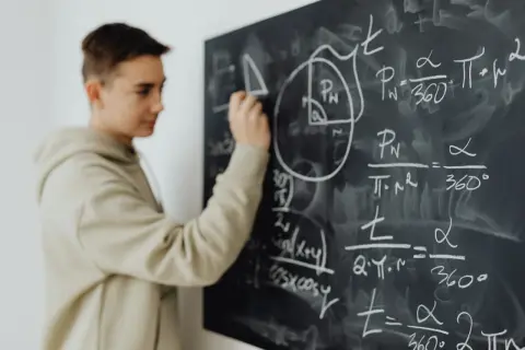 Chłopak rozwiązuje zadania z matematyki na tablicy. W 4 klasie liceum przedmioty takie jak matematyka stają się kluczowe.