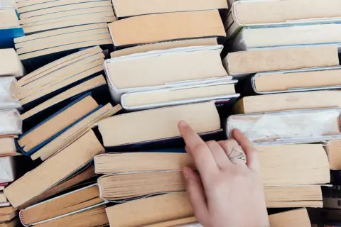 Stos książek, wśród nich cke lektury obowiązkowe. Dłoń z pierścionkiem sięga po jedną z nich.
