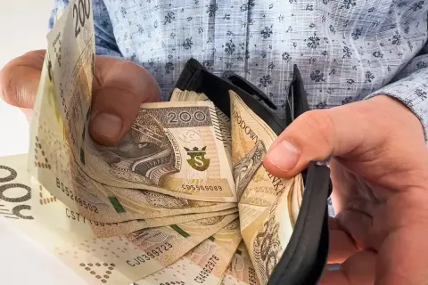 Ręce trzymają portfel z banknotami 200 zł. To symbol nagrody jubileuszowej za 40 lat pracy w budżetówce.