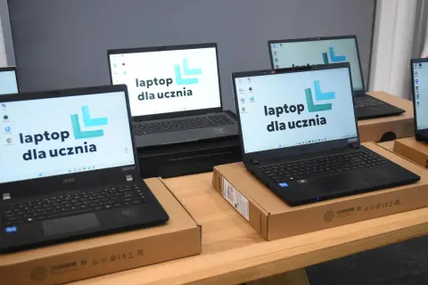 Kilka laptopów z logo "laptop dla ucznia" na ekranach, gotowych do przekazania uczniom.