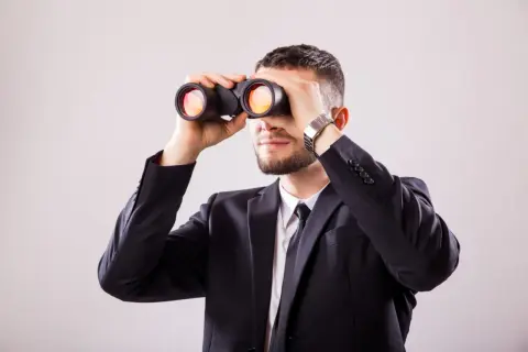 Mężczyzna w garniturze przez lornetkę szuka odpowiedzi na pytanie: wakat co to.