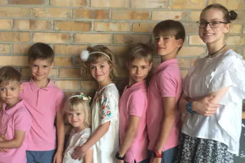 Szczęśliwa rodzina wielodzietna pozuje do zdjęcia na tle ceglanej ściany.