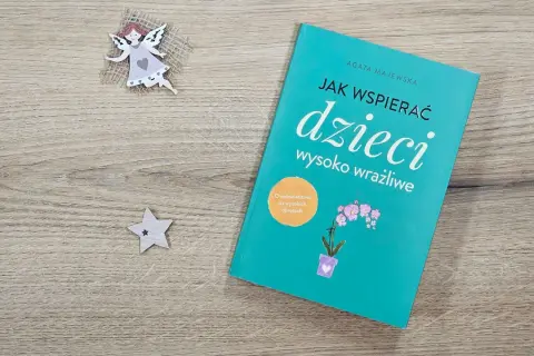 Książka "Jak wspierać dzieci wysoko wrażliwe" na drewnianym tle, obok aniołka i gwiazdki.