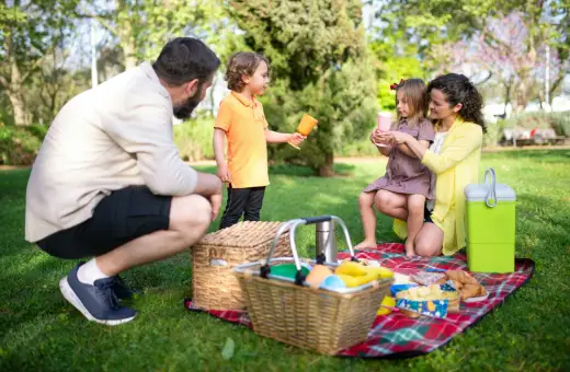 Radosny piknik rodzinny w parku. Rodzice i dzieci cieszą się wspólnym czasem na kocu, wśród zieleni.