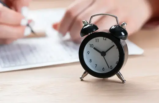 Budzik obok arkusza egzaminacyjnego. Czas na rozwiązanie zadań z matematyki ósmoklasisty mija.