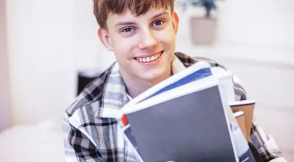 Uśmiechnięty student z książkami, zastanawia się, jak rozliczyć dochody dziecka pełnoletniego uczącego się.