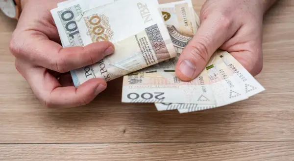 Ręce liczą banknoty 100 i 200 zł. To pieniądze na wymarzone wczasy pod gruszą, by odpocząć od codzienności.