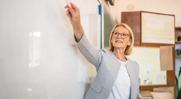 Nauczycielka z markerem przy tablicy, ocena pracy nauczyciela początkującego.