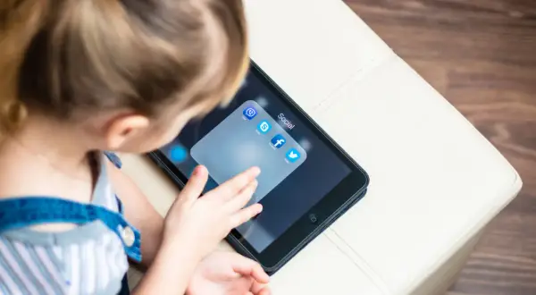Dziecko dotyka ekranu tabletu z ikonami aplikacji społecznościowych, w tym Facebooka. Od ilu lat można mieć Facebooka?