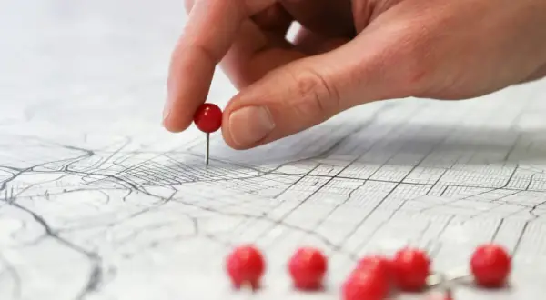 Dłoń z czerwonym pinezką na mapie miasta, ilustrującej różne rodzaje map i ich zastosowania.