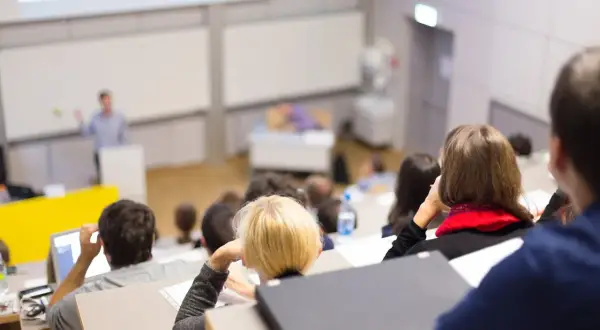 Nauczyciel akademicki prowadzi wykład w auli, studenci słuchają, niektórzy notują.