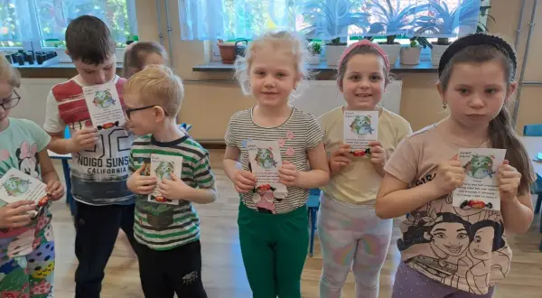 Dzieci z oddziału przedszkolnego świętują Dzień Ziemi, trzymając w rękach kartki z motywem planety i słodkości.