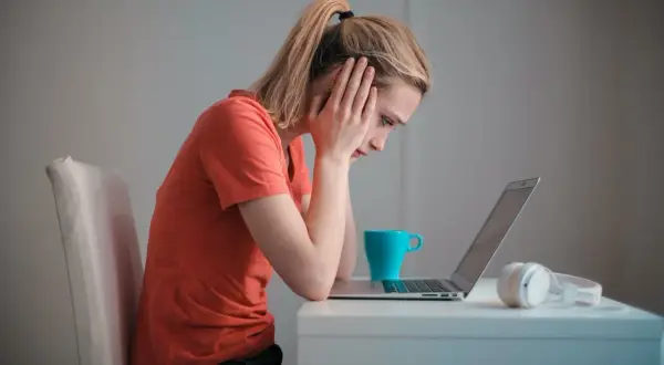 Zmartwiona dziewczyna z rękami na skroniach patrzy na laptopa. Może to być związane z zawieszeniem w prawach ucznia.