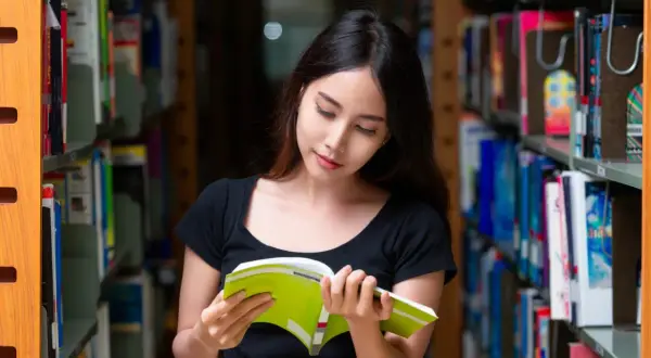 Młoda kobieta w bibliotece, pochłonięta lekturą. Czy jej oceny pozwolą jej uzyskać stypendium?