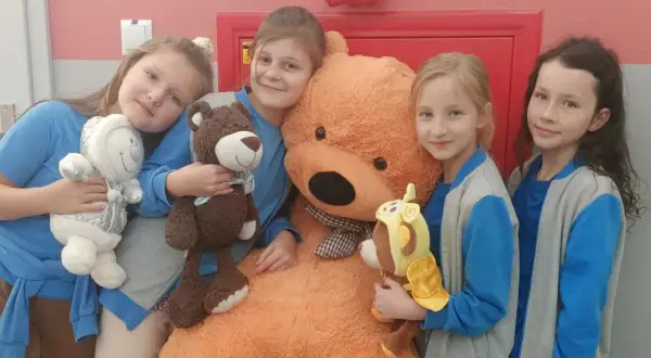 Cztery dziewczynki świętują dzień misia, przytulając pluszowe misie, w tym jednego gigantycznego.