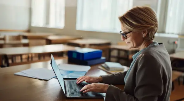 Kobieta w okularach pracuje na laptopie w pustej sali lekcyjnej. Może szukać informacji o studiach podyplomowych online bezpłatnych.