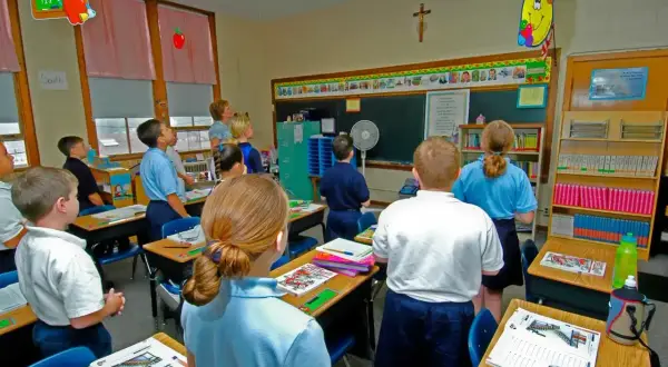 Dzieci w szkole katolickiej słuchają katechety.