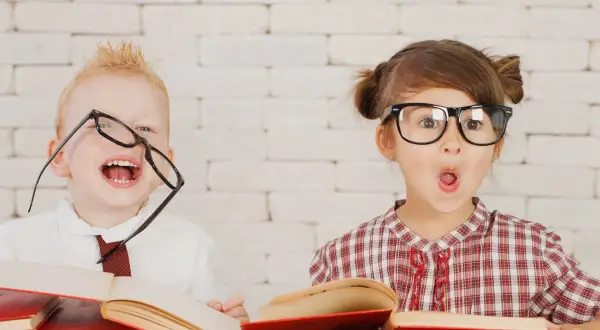 Dzieci z okularami i książkami, wesołe i zaskoczone. Wczesna pedagogika w praktyce, rozbudzająca ciekawość świata.
