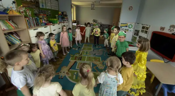 Dzieci trzymają się za ręce w kręgu na dywanie z zabawnymi zwierzątkami. To radosny dzień w **zespole szkolno przedszkolnym**.