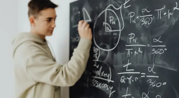Chłopak rozwiązuje zadania z matematyki na tablicy. W 4 klasie liceum przedmioty takie jak matematyka stają się kluczowe.