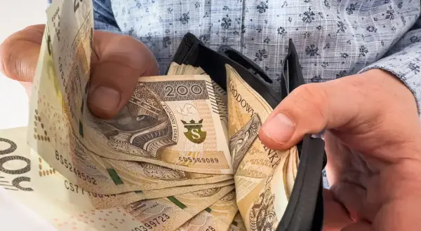 Ręce trzymają portfel z banknotami 200 zł. To nagroda jubileuszowa za 15 lat pracy, symbol docenienia za lata zaangażowania.