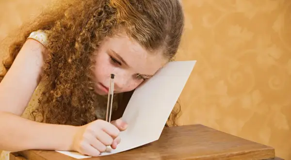 Dziewczynka z kręconymi włosami i piegami z trudem pisze, walcząc z dysleksją rozwojową.