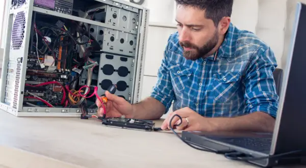 Mężczyzna, jako **technik informatyk**, naprawia komputer, podłączając dysk twardy.