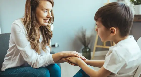 Kobieta wspiera chłopca, trzymając go za ręce. Rozmowa o wydłużeniu etapu edukacyjnego, budowanie pewności siebie.